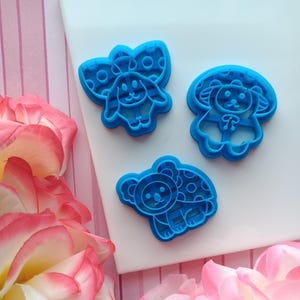 May include: Three blue plastic cookie cutters shaped like animals with polka dots. The cutters are on a white surface.