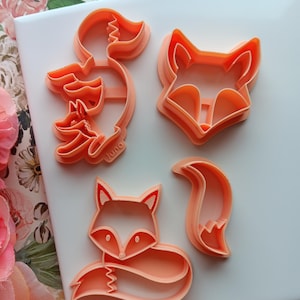 May include: A set of four orange plastic cookie cutters shaped like foxes. The cutters include a fox head, a fox body, a fox tail, and a fox with a baby fox inside.