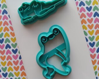 Puede incluir: Dos cortadores de galletas de plástico azul turquesa, uno con forma de rana y el otro con forma de rana tumbada de espaldas.
