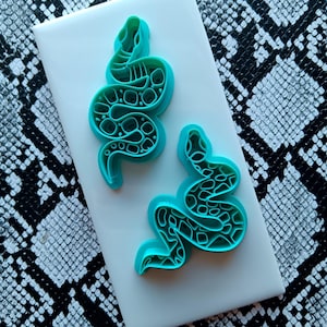 May include: Two turquoise blue snake-shaped cookie cutters on a white background. The snakes have a textured, patterned design.