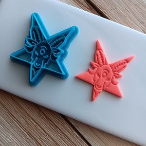 May include: Two star-shaped cookie cutters, one blue and one orange, with a goat head design in the center.