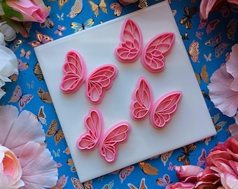 May include: Five pink paper butterfly cutouts on a white background. The butterflies are layered and have a delicate, intricate design.