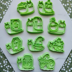 May include: A set of ten light green plastic cookie cutters, each shaped like a snail with a different object on its back, including a cauldron, candle, book, window, potion bottle, coffin, witch hat, house, jar with an eye, and a bearded wizard.