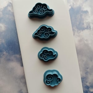 May include: Four blue plastic cookie cutters shaped like clouds with swirling designs.