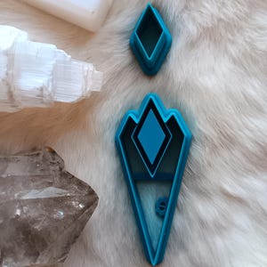 May include: Two blue plastic cookie cutters shaped like diamonds. The larger cutter has a smaller diamond shape inside.
