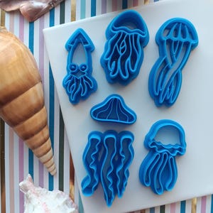 May include: A set of six blue plastic cookie cutters shaped like sea creatures. The cutters include a squid, a jellyfish, and a starfish.