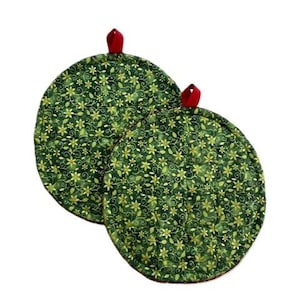 May include: Two round quilted pot holders featuring a dark green fabric base with a repeating pattern of gold-colored flowers and swirling vines. Each pot holder includes a small red fabric loop at the top for hanging, providing a functional design.