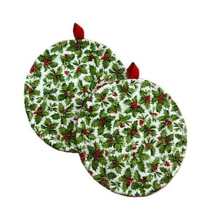 May include: Two round pot holders featuring a white background with a repeating pattern of green holly leaves and red berries. Each circular pot holder includes a small red fabric loop at the top for hanging, designed with a quilted texture.
