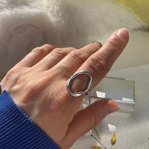 Puede incluir: Un anillo de plata con un diseño abstracto de forma ovalada. El anillo se lleva en el dedo índice de una mano.
