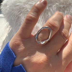 Peut inclure: Une bague en argent avec un design abstrait de forme ovale. La bague est portée à un doigt.