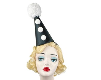 May include: A black and white party hat with a white pom-pom on top. The hat has three white polka dots on the front. A mannequin with blonde hair is wearing the hat.