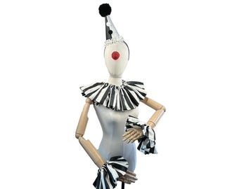 May include: A white and black striped clown collar with a black and white striped cuff. The collar and cuff are on a mannequin with a red clown nose and a black and white striped hat.