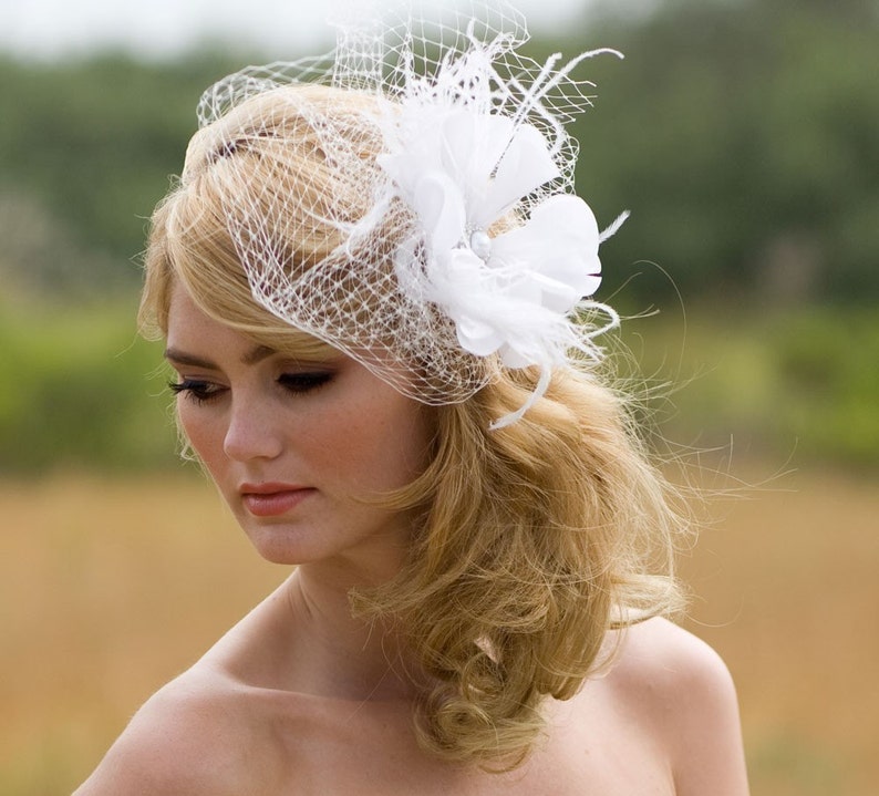 May include: A bride with blonde hair wearing a white veil with a flower accent.