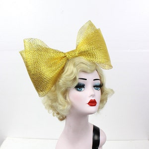 May include: A large gold mesh bow hair accessory. The bow is made of a sparkly gold mesh fabric and is tied in a large, dramatic bow.