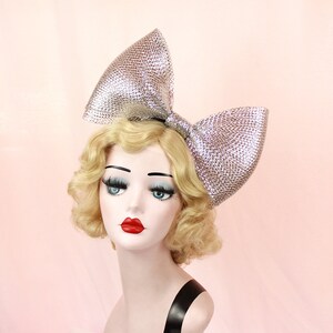 May include: A large silver sparkly bow headband. The bow is made of a shiny material and is very large. It is a statement piece that would be perfect for a party or special occasion.