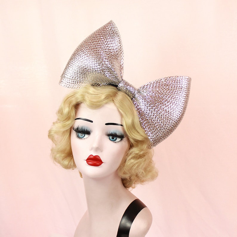May include: A large silver sparkly bow headband. The bow is made of a shiny material and is very large. It is a statement piece that would be perfect for a party or special occasion.