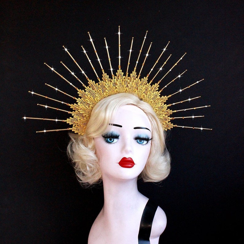 May include: A gold crown with a sunburst design. The crown is made of metal and has a delicate, intricate design. The crown is adorned with small, sparkling rhinestones.