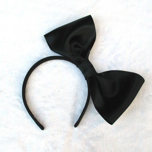 May include: A black satin headband with a large black bow. The headband is made of a thin, flexible material and is designed to fit comfortably on the head.