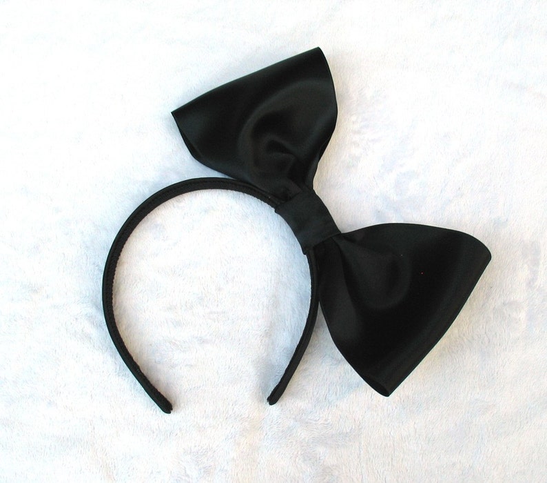 May include: A black satin headband with a large black bow. The headband is made of a thin, flexible material and is designed to fit comfortably on the head.