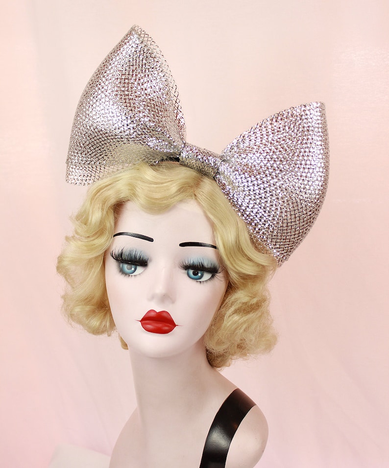 May include: A large silver sparkly bow headband. The bow is made of a mesh material and is very large, covering most of the head.