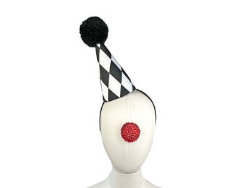 May include: A white and black checkered party hat with a black pom-pom on top. The hat is worn on a white mannequin head with a red clown nose.