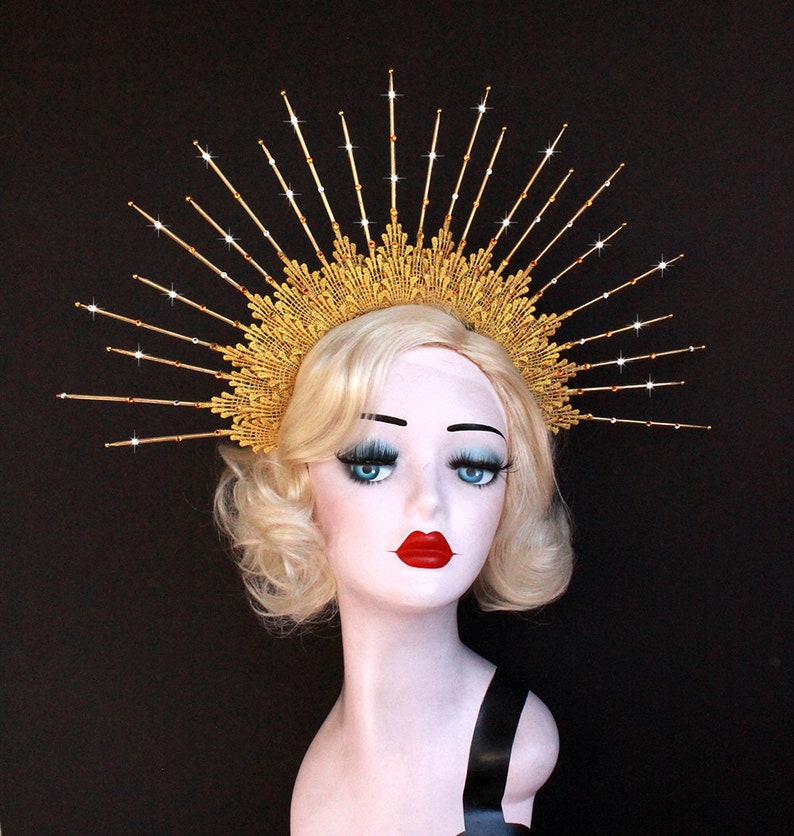 May include: A gold crown with a sunburst design and clear rhinestones. The crown is made of metal and has a delicate, intricate design.