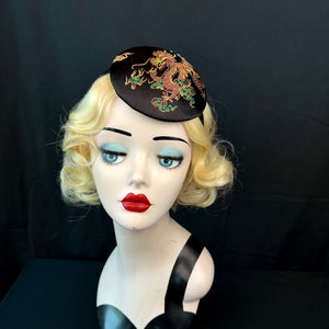 May include: A black satin hat with a gold and green embroidered dragon design.