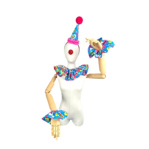 May include: A white mannequin wearing a blue and pink clown costume with a pink and white hat. The costume has a ruffled collar and matching wrist cuffs. The mannequin has a red clown nose.