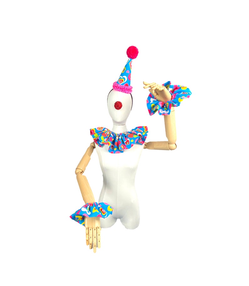 May include: A white mannequin wearing a blue and pink clown costume with a pink and white hat. The costume has a ruffled collar and matching wrist cuffs. The mannequin has a red clown nose.