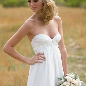 May include: A bride wearing a white strapless wedding dress with a white flower and veil headpiece. She is holding a bouquet of white flowers with green leaves.