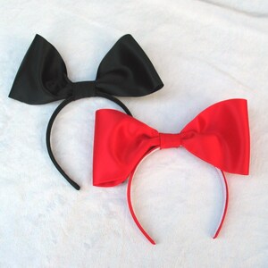 May include: Two hair headbands with large satin bows. One headband has a black bow and the other has a red bow.