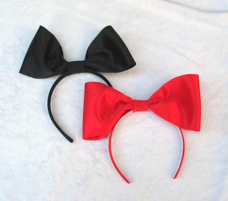 May include: Two hair headbands with large satin bows. One headband has a black bow and the other has a red bow.
