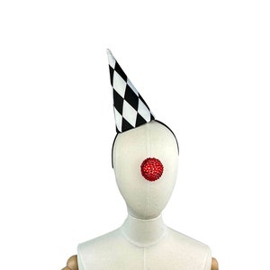 May include: A white mannequin head wearing a black and white checkered party hat and a red clown nose.