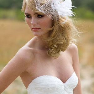 May include: A bride wearing a white strapless gown with a white birdcage veil and a white flower hairpiece.