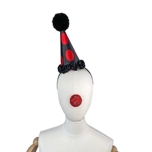 May include: A black and red clown hat with a black pom-pom on top. The hat has red polka dots and a black ruffle around the base. A red jeweled clown nose is attached to a white mannequin head.