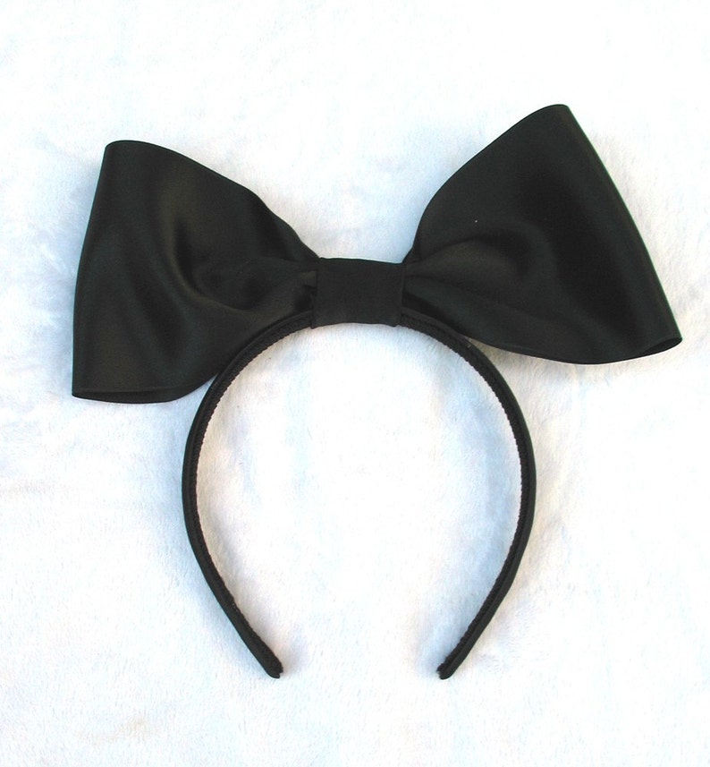 May include: A black satin bow headband. The headband is made of a thin black elastic band and has a large black satin bow attached to it.