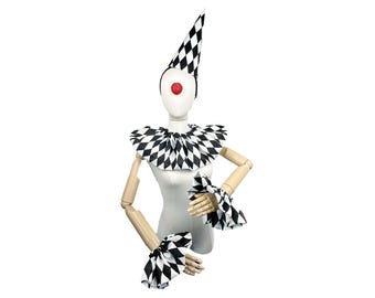 Puede incluir: Un conjunto de disfraz de bufón a cuadros blanco y negro con sombrero, cuello y puños. El sombrero es puntiagudo y tiene un patrón a cuadros blanco y negro. El cuello es de volantes y los puños también son a cuadros.