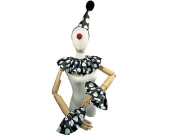 Puede incluir: Un conjunto de disfraz de payaso sobre un maniquí. El conjunto incluye un sombrero de lunares blancos y negros con un pompón negro, un cuello con volantes y puños a juego. Se adjunta una nariz roja. El disfraz está diseñado para una ocasión festiva.