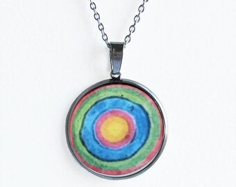 May include: A silver chain necklace with a round pendant featuring a colorful concentric circle design. The pendant has a silver rim and a glass-like surface. The colors in the design are red, pink, yellow, blue, and green.