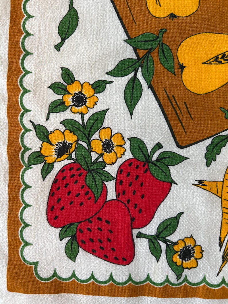 May include: A vintage white kitchen towel with a repeating pattern of red strawberries, yellow flowers, and green leaves. The towel has a brown border with a scalloped edge. The design also includes yellow apples.