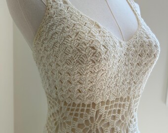 Könnte beinhalten: Cremefarbenes Häkelkleid mit V-Ausschnitt und Lochmusterdetails. Das Kleid wird auf einer Schaufensterpuppe präsentiert, die die komplizierten Stichmuster und das Gesamtdesign zeigt. Das Kleid hat ein figurbetontes Oberteil und einen ausgestellten Rock.