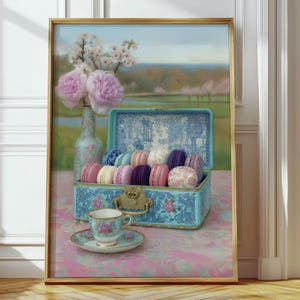 May include: A framed still life painting showing a blue box filled with colourful macarons. A teacup and saucer are in front of the box. A vase of pink flowers and a bottle are behind the box. The painting has a gold frame.