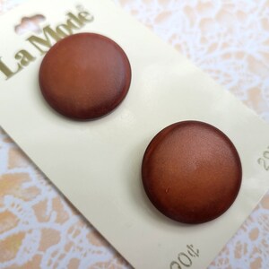 May include: Two brown round buttons with a smooth, slightly shiny finish. The buttons are on a white card with the text "La Mode" and "2972" printed on it.