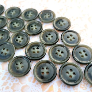 May include: A collection of twenty-one dark gray buttons with four holes each. The buttons have a slightly marbled appearance and a subtle sheen. The buttons are round and appear to be made of plastic or a similar material.