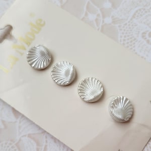 May include: Four silver-colored buttons with a textured, fan-like design are displayed on a white card. The card has the text "La Mode" and the number "46417". The buttons are round and have a slightly raised, ridged pattern.