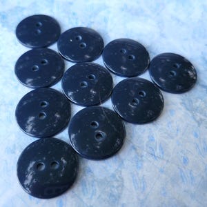 May include: A collection of ten round, dark navy blue buttons arranged in a triangular formation. Each button features a smooth, glossy surface with subtle, lighter blue marbled or speckled patterns and two central holes for attachment.
