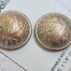 May include: Two round buttons with a metallic finish featuring a textured, copper-toned surface with silver-colored accents. The buttons are attached to a white card displaying the text la-belle and the measurement 1 1/8 inch (28mm).
