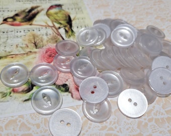 May include: A pile of white pearl buttons with two and four holes. The buttons are arranged in a random pattern and are all the same size.