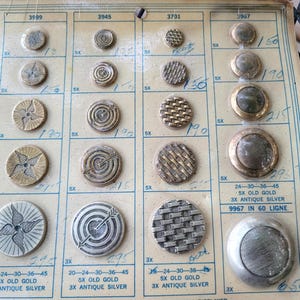 May include: A card with a variety of buttons in gold and silver. The buttons are arranged in rows and columns, and each button has a different design. The card also includes the numbers 3999, 3945, 3701, 3967, and 9967, as well as the text "20-24-30-36-45 5X OLD GOLD 3X ANTIQUE SILVER" and "24-30-36-45 5X OLD GOLD 3X ANTIQUE SILVER".