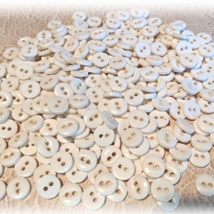 May include: A large pile of white plastic buttons with two holes each. The buttons are round and smooth.